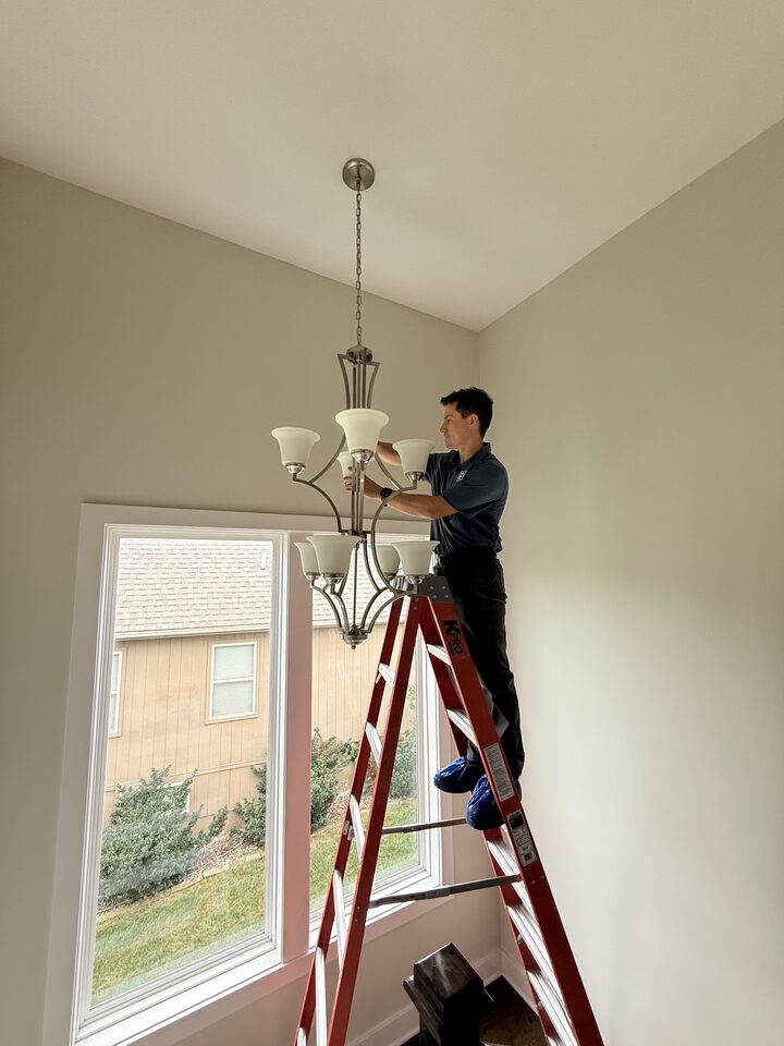 ZV Electric technician servicing a chandelier on a ladder in a residence
